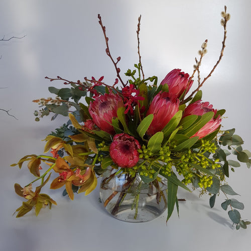 Glass vase of native and premium blooms, including protea, John storey orchids and cymbidium